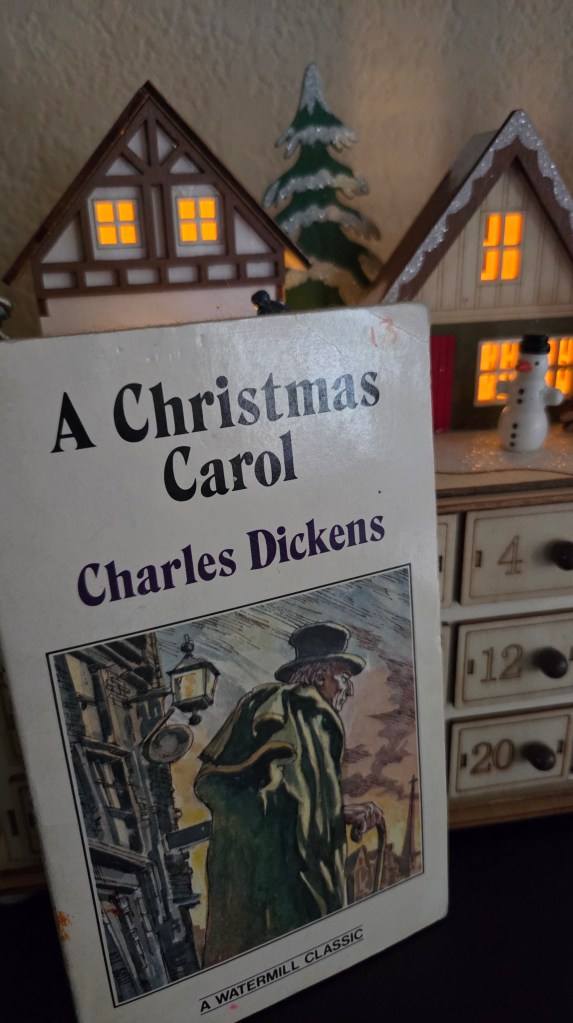the paperback version of A Christmas Carol in front of a holiday decoration